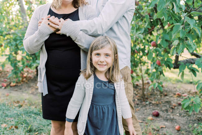 Una niña feliz parada frente a sus padres - foto de stock