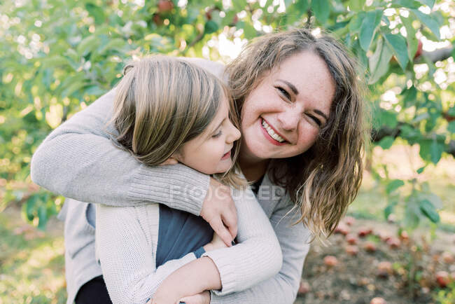 Uma mãe dando à filha um abraço com árvores de maçãs nas costas — Fotografia de Stock