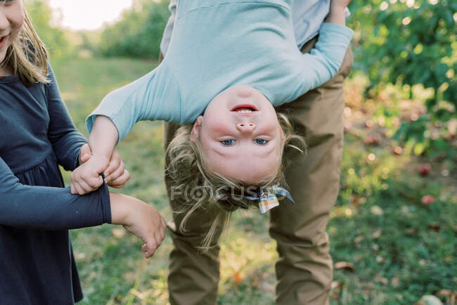 Una linda niña siendo sostenida boca abajo con su hermana animando - foto de stock