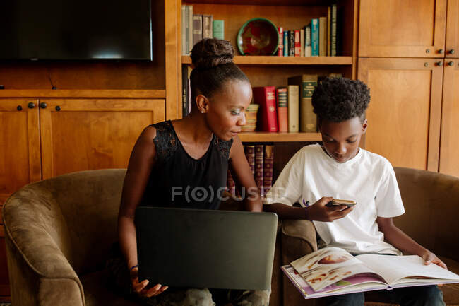 Negro mamá con portátil ayudando a hijo preadolescente durante el aprendizaje a distancia - foto de stock