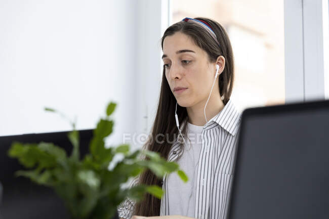Sérieuse jolie femme utilisant un ordinateur portable et des écouteurs dans le bureau moderne — Photo de stock