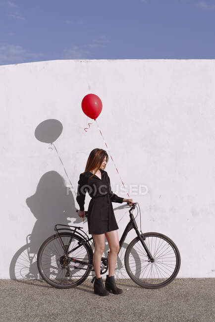 Bicyclette jeune femme portant un ballon de gaz rouge — Photo de stock