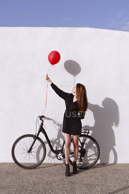 Bicyclette jeune femme portant un ballon de gaz rouge — Photo de stock