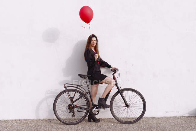 Bicycle young woman wearing a red gas balloon — Stock Photo