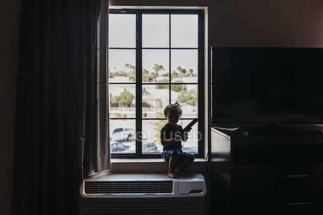 Jeune garçon tout-petit assis dans la fenêtre de la chambre d'hôtel à Palm Springs — Photo de stock