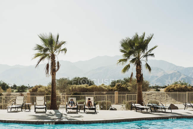 Vue paysage de jeunes frères dans des chaises de piscine avec des montagnes derrière — Photo de stock