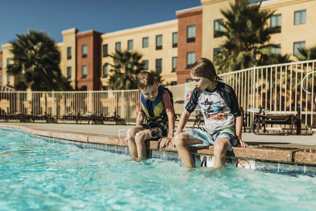 Giovani fratelli seduti uno accanto all'altro a bordo piscina in vacanza — Foto stock