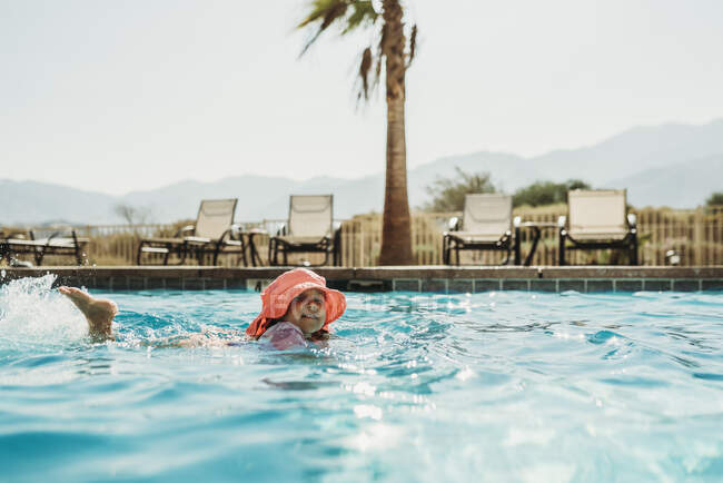 Вид сбоку маленькой девочки в розовой шляпе, плавающей в бассейне — стоковое фото