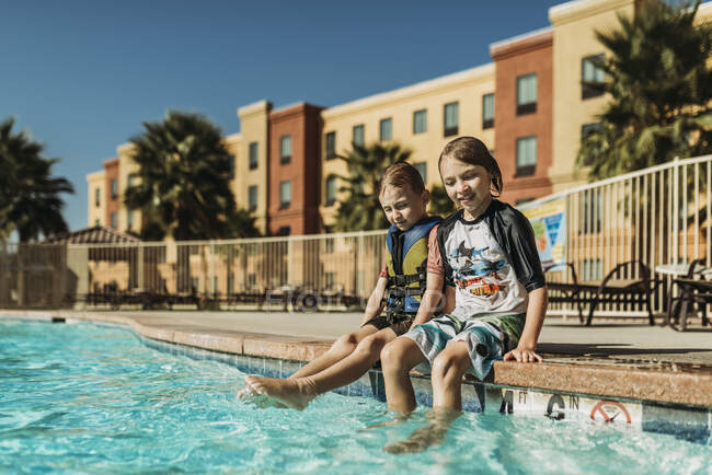 Giovani fratelli seduti uno accanto all'altro a bordo piscina in vacanza — Foto stock