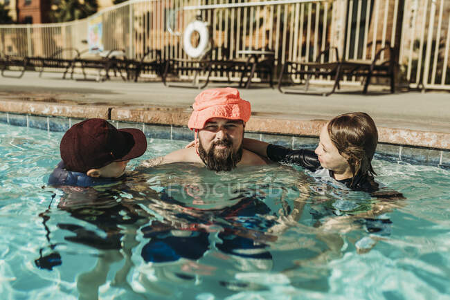 Imagen divertida de papá en sombrero de niño jugando en la piscina con hijos - foto de stock