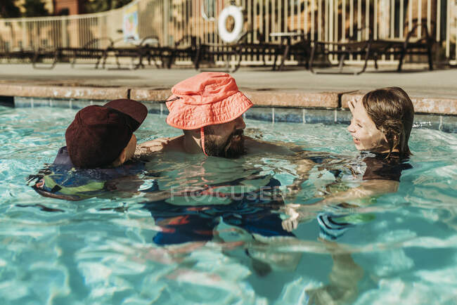 Imagen divertida de papá en sombrero de niño jugando en la piscina con hijos - foto de stock