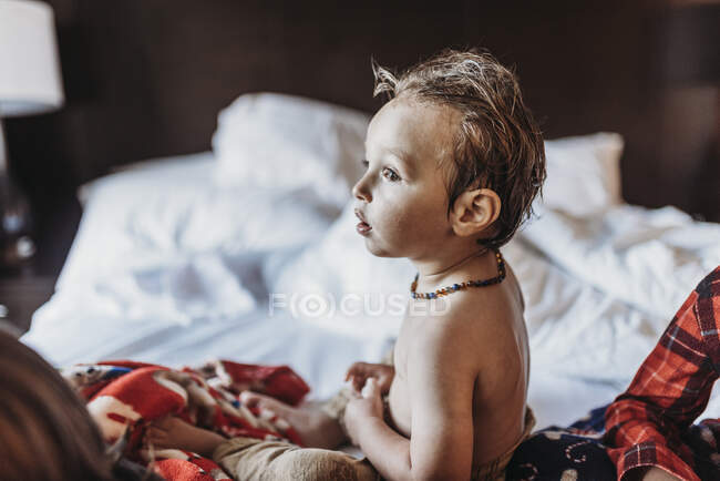 Side view portrait of toddler boy sitting in hotel bed on vacation — Stock Photo