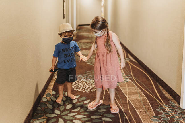 Young siblings wearing masks walking through hotel hallway together — Stock Photo