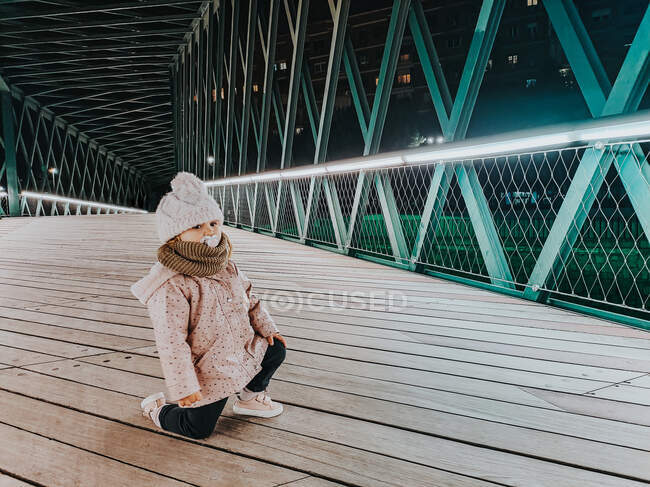 Маленькая девочка с пустышкой позирует на мосту ночью — стоковое фото