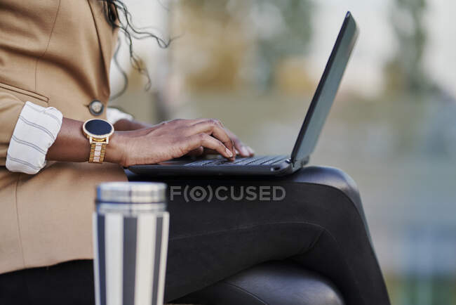 Dettaglio di una donna di colore in un abito marrone che lavora sul suo computer portatile seduto sulla strada — Foto stock