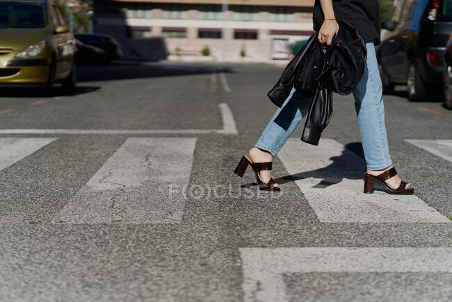 Femme marchant sur un passage à niveau en zèbre portant des talons hauts tenant une veste — Photo de stock
