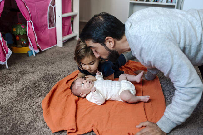 Папа и дочь общаются с младенцем на оранжевом одеяле — стоковое фото