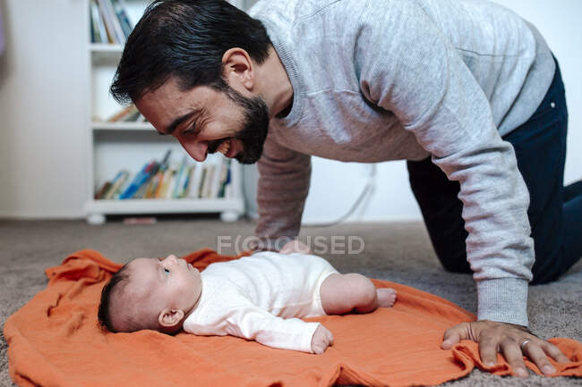 Улыбающийся папа с бородой играет с дочкой на оранжевом одеяле — стоковое фото