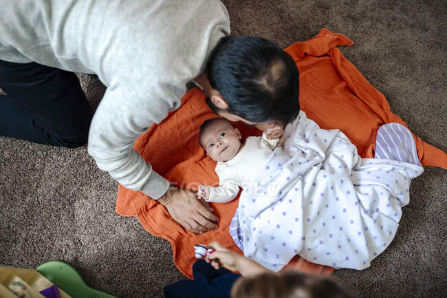 Отец наклоняется над ребенком на оранжевом одеяле на полу — стоковое фото