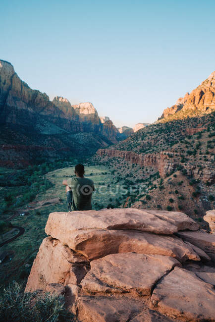 Homem negro montado em uma rocha contemplando a montanha durante o pôr do sol — Fotografia de Stock