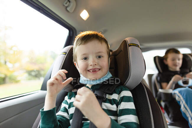Elementary Age Boy sonriendo mientras está sentado en el coche con máscara facial - foto de stock