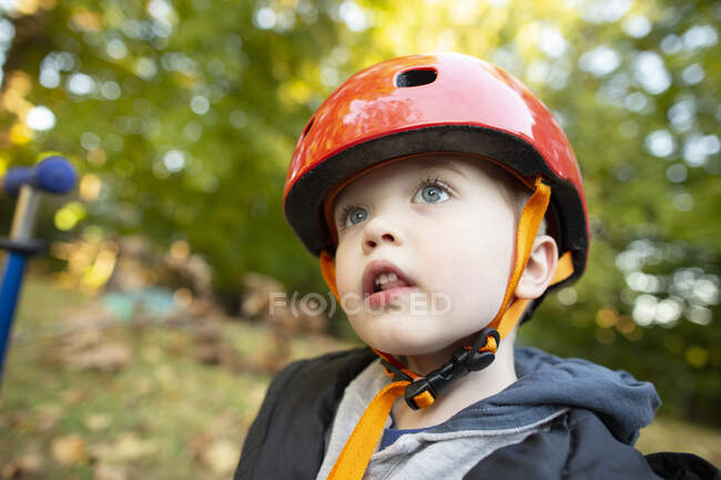 Мальчик дошкольного возраста в красном шлеме смотрит вверх во время игры на улице — стоковое фото