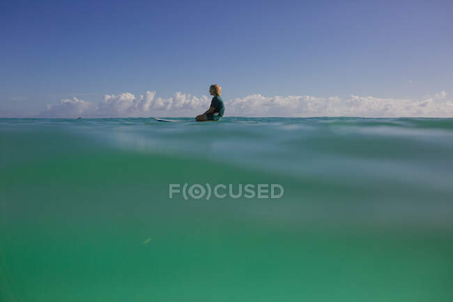Boy rests on a paddleboard on a calm day with turquoise water. — Stock Photo