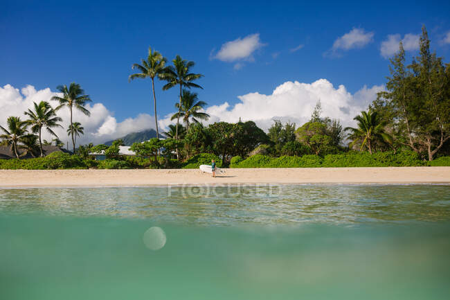 Tween niño lleva un paddleboard al océano en un día tranquilo en Hawaii - foto de stock
