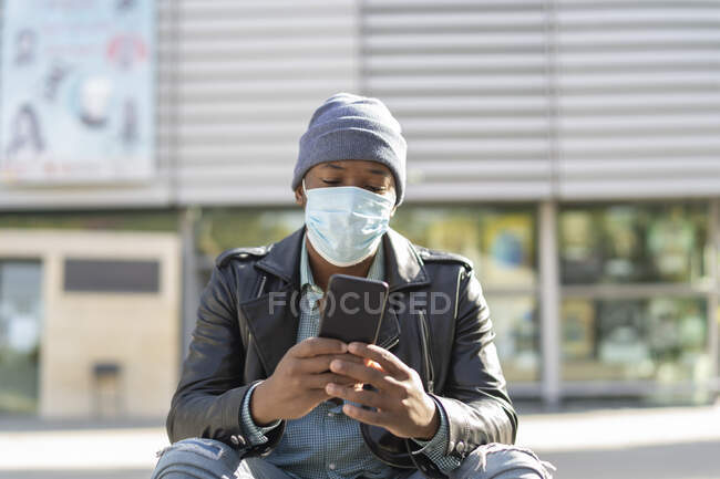 Junger afrikanischer Mann in der Stadt sendet eine Nachricht von seinem Smartphone — Stockfoto