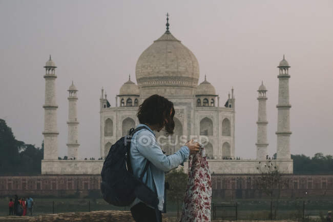 Junge Backpackerin kleidet ihre Pashmina, bevor sie Mehtab Bagh verlässt, mit dem Taj Mahal im Hintergrund. — Stockfoto