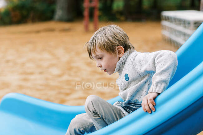 Un niño en un tobogán en el patio de recreo - foto de stock