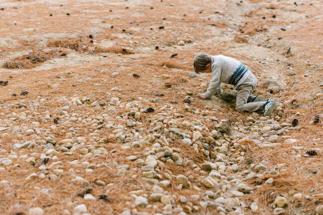 Маленький хлопчик копає в піску за ще камінням. — стокове фото