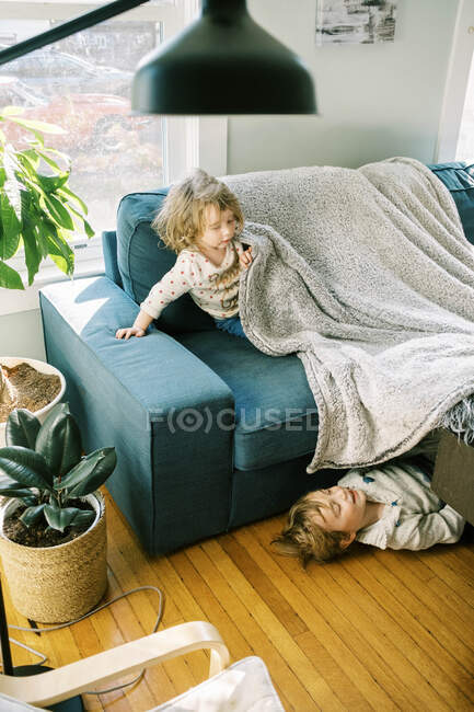 Due bambini che giocano insieme sotto una coperta nel loro salotto — Foto stock
