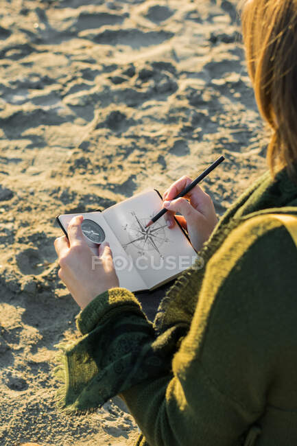 La joven está dibujando una brújula en un cuaderno. Estilo de vida, viajes - foto de stock
