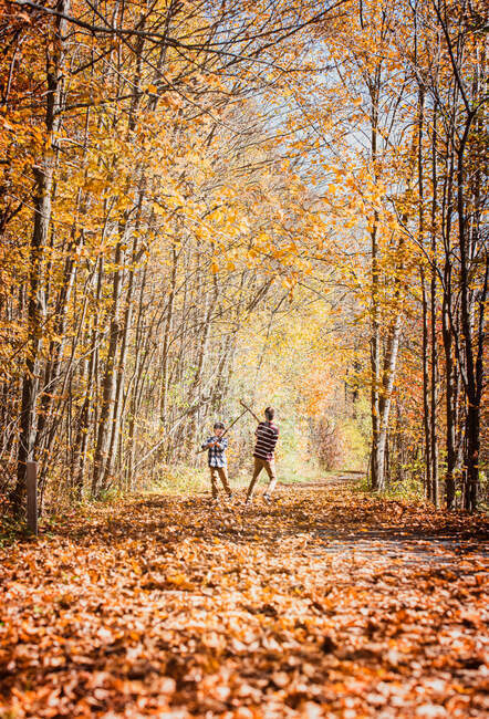 Two boys play fighting with sticks on leaf covered trail in autumn. — Stock Photo