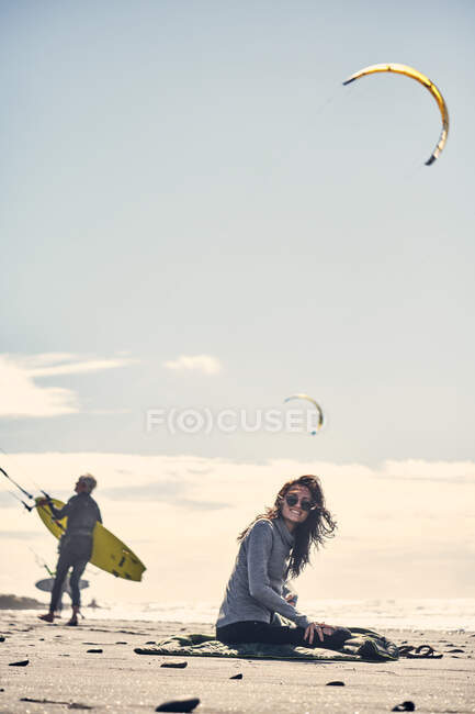Femme s'assoit et regarde cerf-volant surfeurs d'une plage dans le sud de la Califonie — Photo de stock