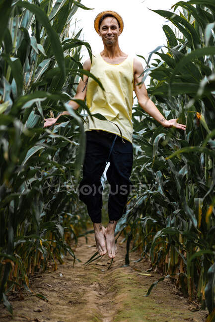 Joven con sombrero recogiendo maíz en un campo de maíz - foto de stock