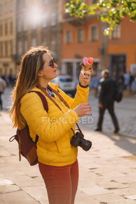 Jeune femme touriste, manger de la crème glacée, heureux, rire, journée ensoleillée, appareil photo touristique. — Photo de stock