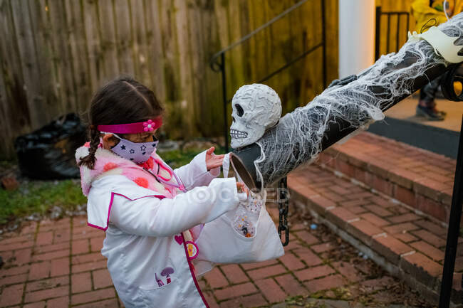 Girl in doctor costume socially distant trick or treating candy chute — Stock Photo