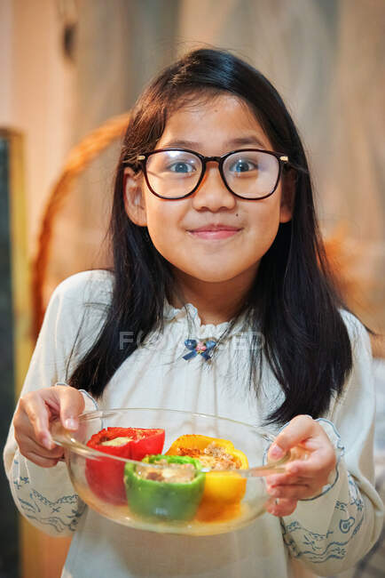 Uma menina mostrando seus pimentões coloridos cozidos na tigela de vidro — Fotografia de Stock