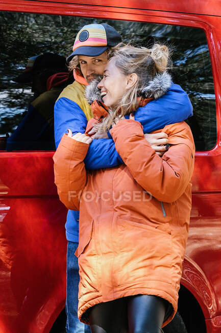 Casal jovem abraçando fora de um campervan vermelho pronto para viajar. aventureiro — Fotografia de Stock