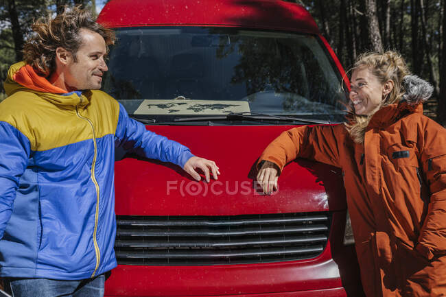 Young couple smiling and staring at each other outside of a red camper — Stock Photo