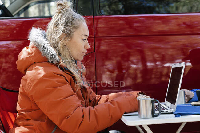 Frau trägt Mantel und arbeitet außerhalb ihres roten Lagers an ihrem Laptop — Stockfoto