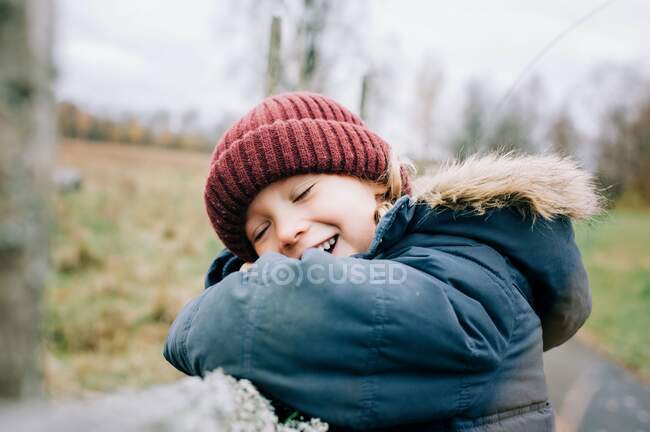 Criança sorrindo inclinada em uma cerca enquanto brincava fora no outono — Fotografia de Stock