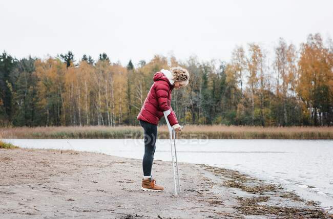 Donna ferita in piedi sulla spiaggia con stampelle cercando premuroso — Foto stock