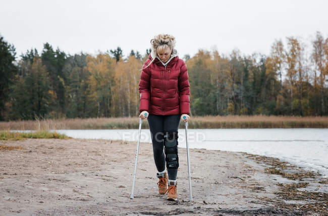 Injured woman walking with crutches on the beach looking thoughtful — Stock Photo