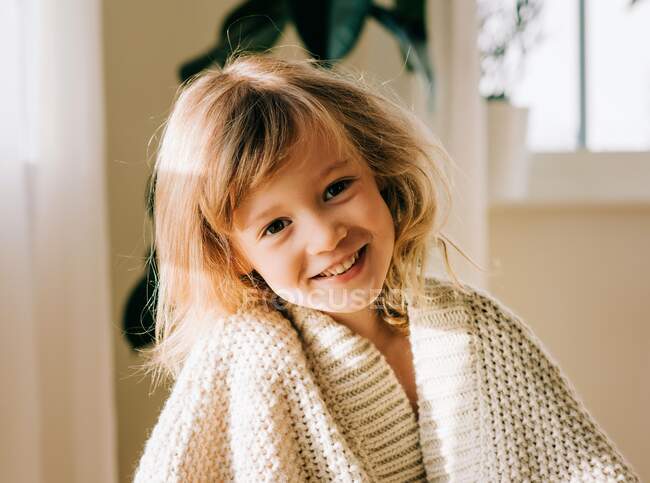Porträt eines lächelnden jungen Mädchens, das zu Hause in eine Decke gehüllt saß — Stockfoto