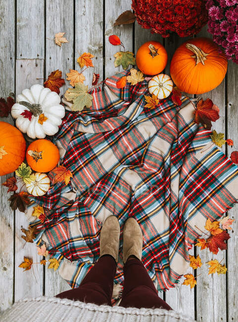 Vue aérienne des pieds de la femme sur l'écharpe à carreaux entourée d'articles d'automne. — Photo de stock