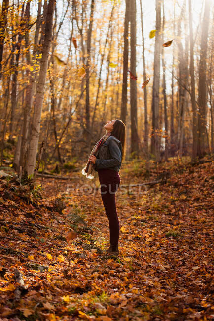 Frau steht an einem Herbsttag im Wald und blickt zu den Bäumen auf. — Stockfoto