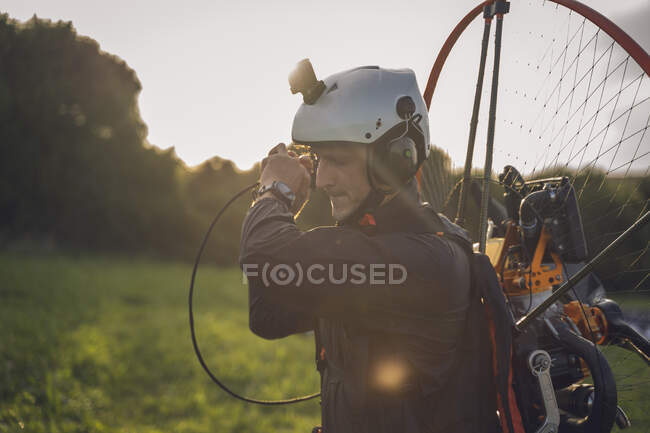Молодий чоловік, з двигуном Powered Paragliding в плечах, готується до польоту, на заході сонця, тягнучи мотузку, щоб почати двигун. — стокове фото
